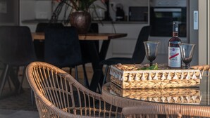 Un coin repas avec des chaises en osier, une table en verre et une bouteille de vin.