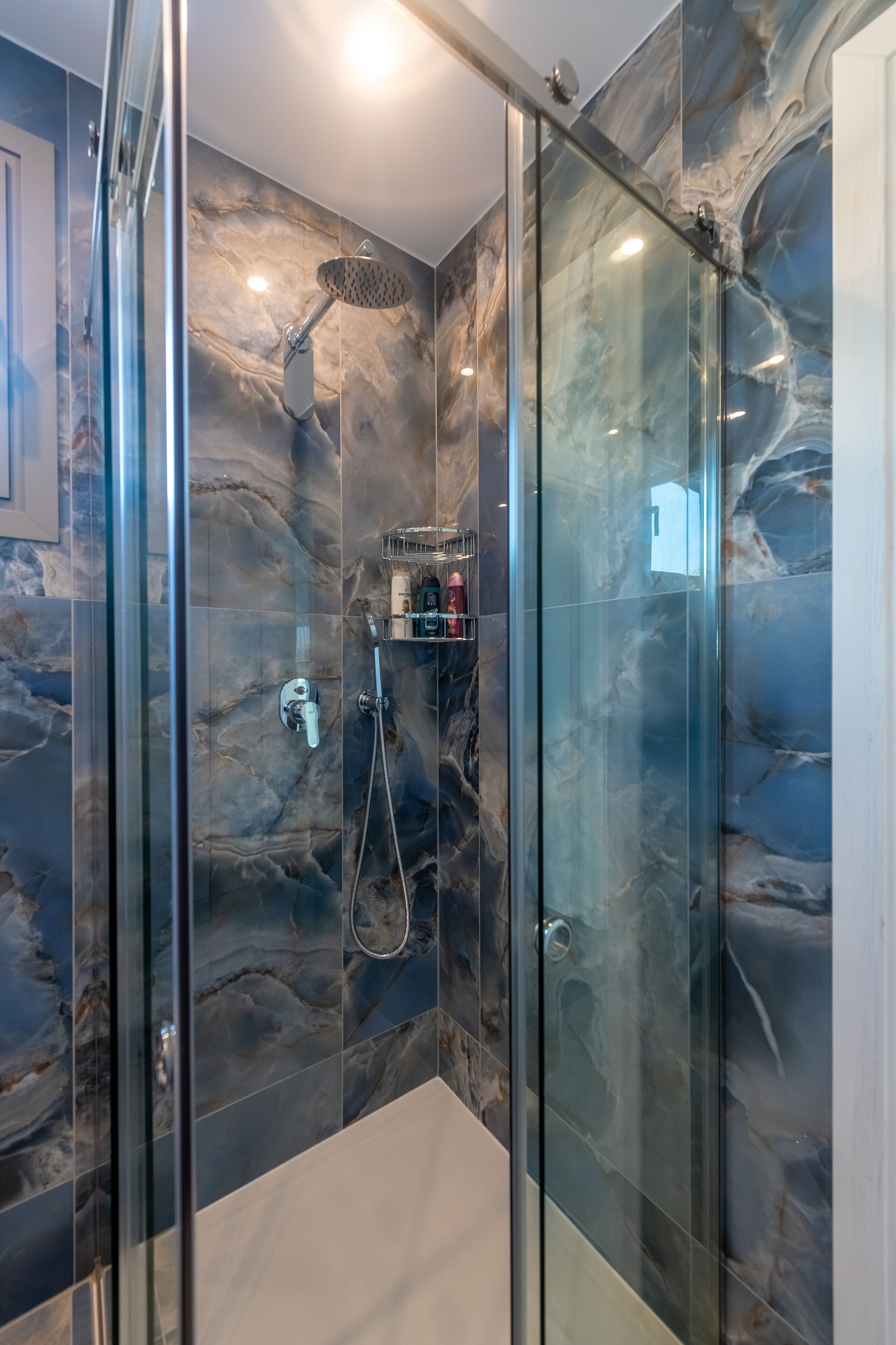 A modern shower with glass doors, marble walls, and a handheld showerhead.