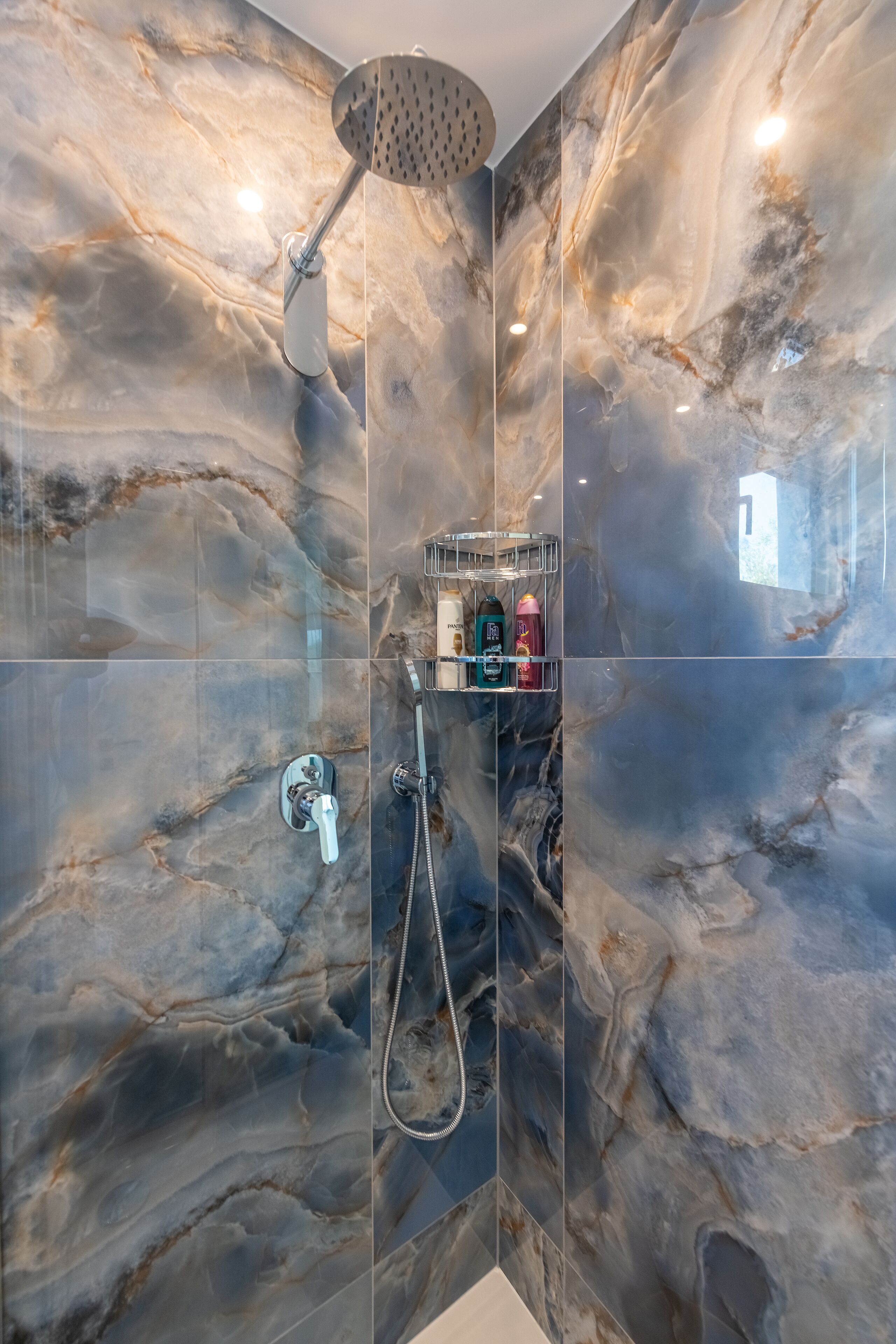 Een moderne badkamer met een douche, een wastafel met glazen kast en een marmeren spatwand.