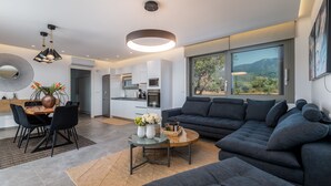 Un salon moderne avec un canapé gris foncé, une table basse en verre et un coin repas comprenant une table et des chaises en bois.