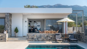Une maison moderne dotée d’une piscine, de murs en pierre et d’un patio aménagé avec du mobilier d’extérieur.
