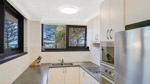 A modern kitchen with white cabinets, a stainless steel refrigerator, and a window with a view of trees and the ocean. - Porta Pacifique 3 - Renovated Beachfront Bilinga (Bilinga)