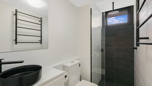 A modern bathroom with a glass shower enclosure, a black towel rack, and a white toilet. - Porta Pacifique 3 - Renovated Beachfront Bilinga (Bilinga)