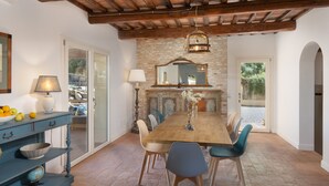 A dining area with a wooden table, chairs, a lamp, and a stone wall.