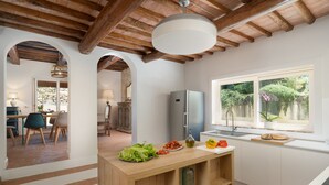 A modern kitchen with a wooden island, a refrigerator, and a window with a view of greenery.
