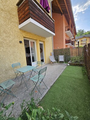 En bostadsbyggnad med en balkong, en uteplats med utemöbler och en välskött gräsmatta.