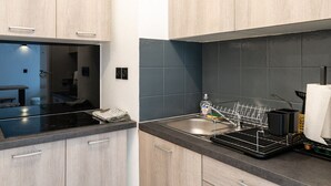 A modern kitchen with wooden cabinets, a black countertop, and a stainless steel sink. - Appartement Maria (Briançon)