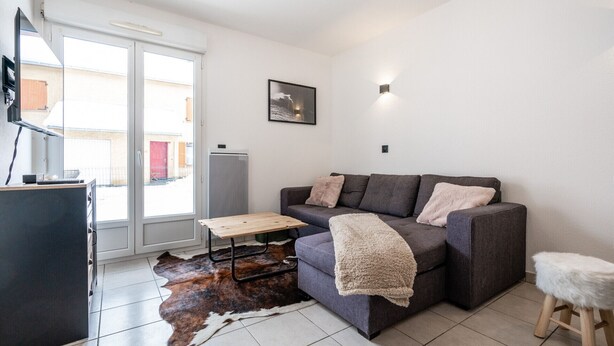 A modern living room with a grey sofa, a wooden coffee table, a leather rug, and a small stool. - Appartement Maria (Briançon)