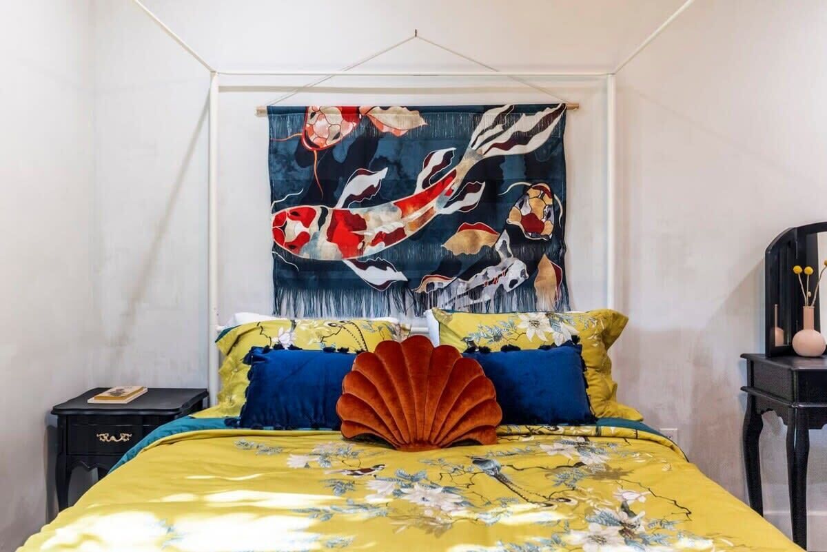 A bedroom with a bed featuring a floral bedspread, blue and yellow pillows, and a large decorative shell.
