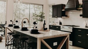 A modern kitchen with a marble island, black bar stools, and dark cabinetry. - Secluded 2-King Suite Cabin w/ Hot Tub, Fireplace & Forest Views (Broken Bow)