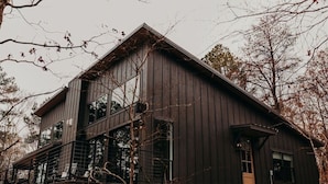 A modern two-story building with large windows and a sloped roof, surrounded by trees. - Secluded 2-King Suite Cabin w/ Hot Tub, Fireplace & Forest Views (Broken Bow)