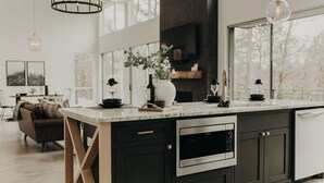 A modern kitchen with a large island, stainless steel appliances, and pendant lighting. - Secluded 2-King Suite Cabin w/ Hot Tub, Fireplace & Forest Views (Broken Bow)
