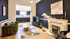 A living room with a green sofa, a coffee table, a fireplace, and a TV.