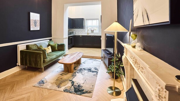 A modern living room with a green sofa, a wooden coffee table, and a fireplace.