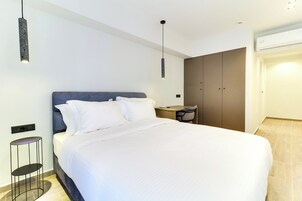 A modern hotel room with a large bed, a bedside table, a chair, a wardrobe, and a hanging light fixture.