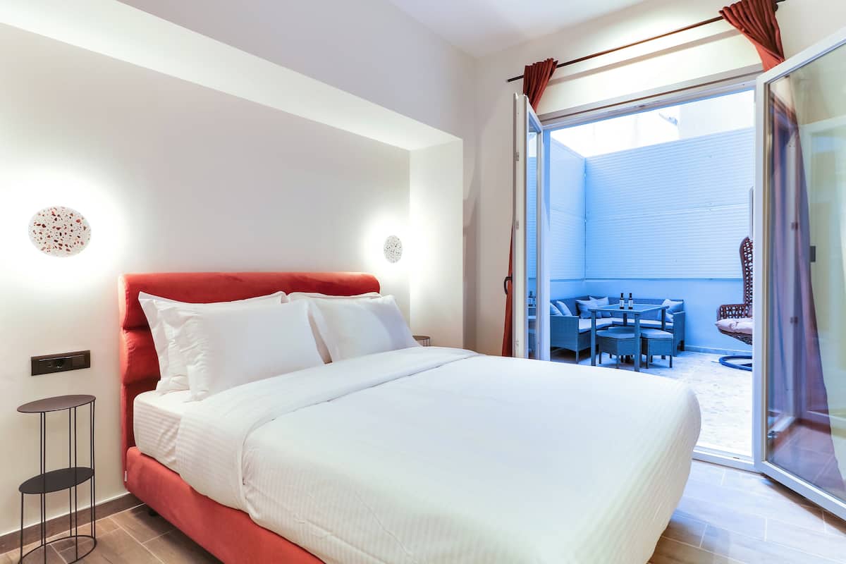 Ein Hotelzimmer mit einem großen Bett, einem kleinen Nachttisch und Blick auf einen Außenbereich durch eine Schiebetür.