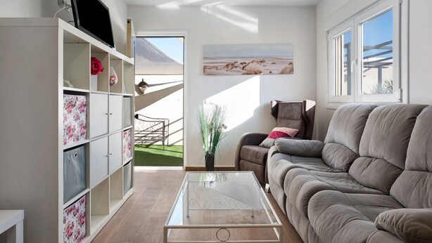 Un salon avec un canapé, une table basse en verre, un téléviseur posé sur un meuble, une bibliothèque et un tableau accroché au mur.