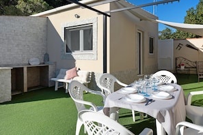 A patio with a table set for dining, outdoor chairs, a stone wall, and a small building with a window.