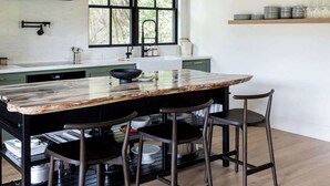 A modern kitchen with a large island, bar stools, and a window with a view of trees. - The Barn Villa (Healdsburg)