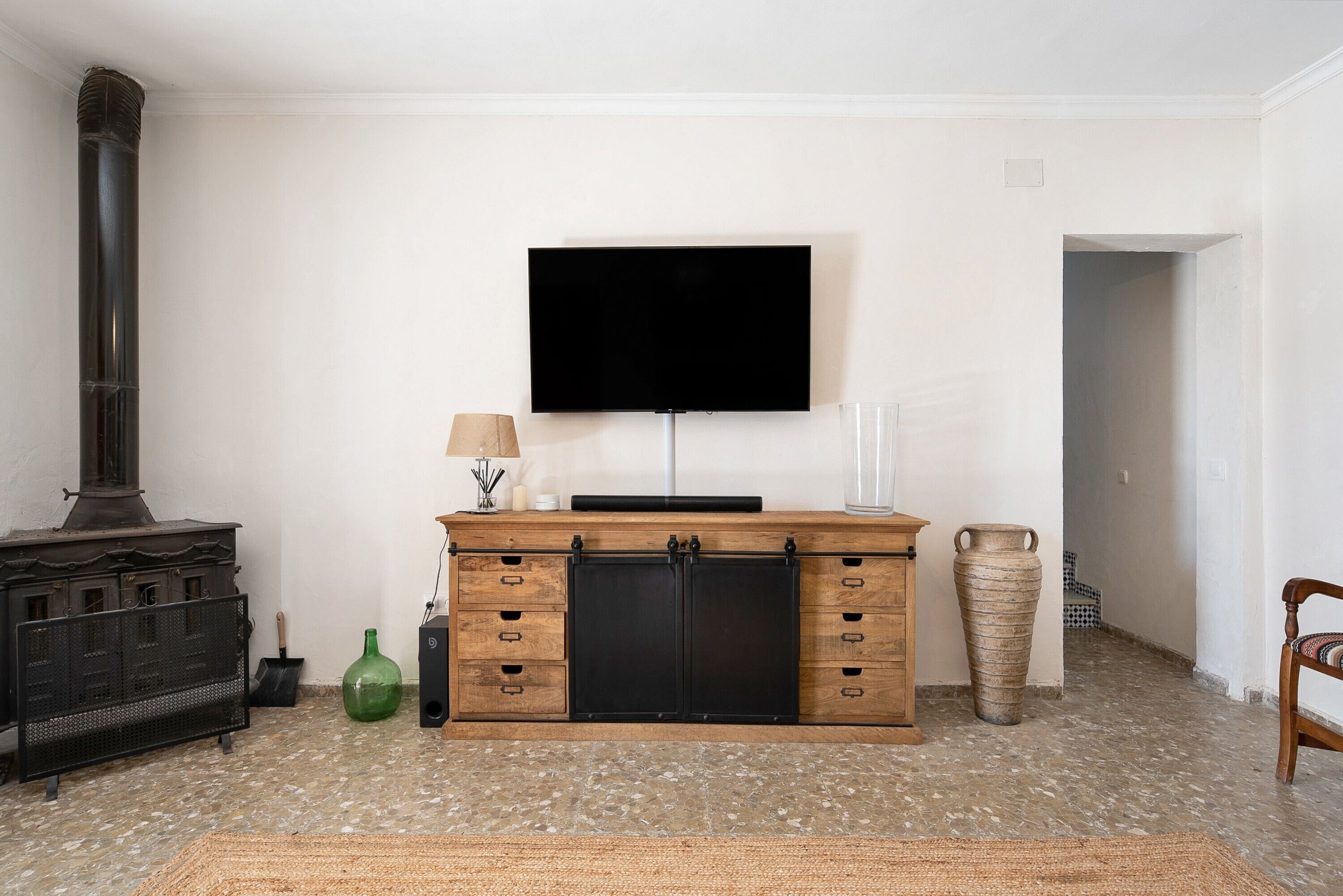 A living room with a fireplace, a television mounted on the wall, a wooden cabinet, and a tiled floor.