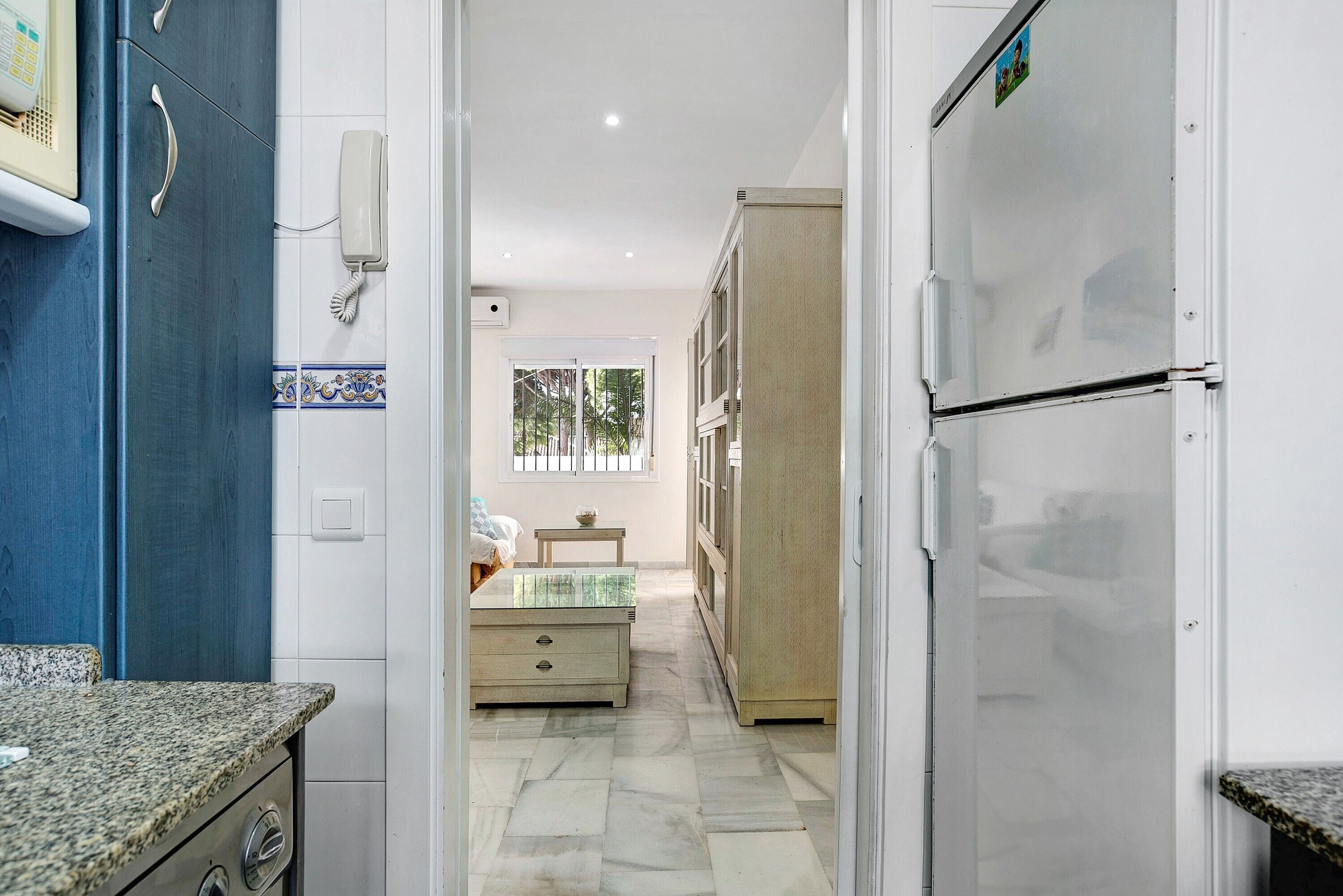 Un pasillo estrecho con una zona de cocina a la izquierda, un refrigerador a la derecha y una cama con una ventana al fondo.
