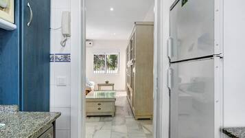 Un pasillo estrecho con una zona de cocina a la izquierda, un refrigerador a la derecha y una cama con una ventana al fondo.
