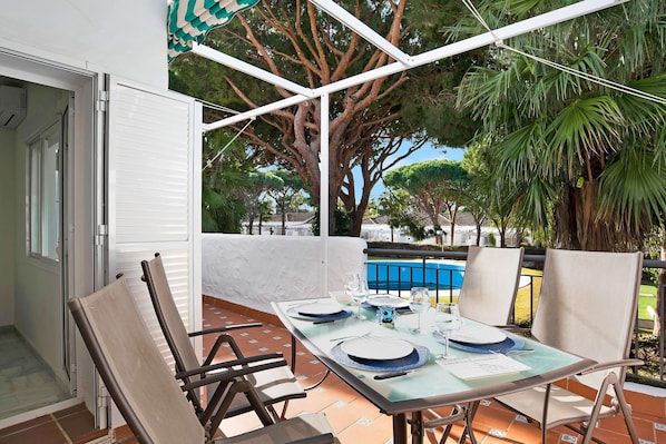 An outdoor dining area with a table set for four, chairs, and a view of a swimming pool and trees.