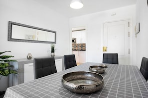 A dining area with a table, chairs, a large mirror, and a kitchen in the background.