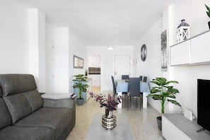 A modern living room with a sofa, a dining table, chairs, a TV, and decorative plants.