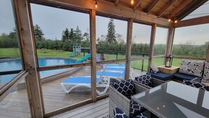 Ett takförsett utomhusområde med en pool, solstolar och en sittgrupp med kuddar.
