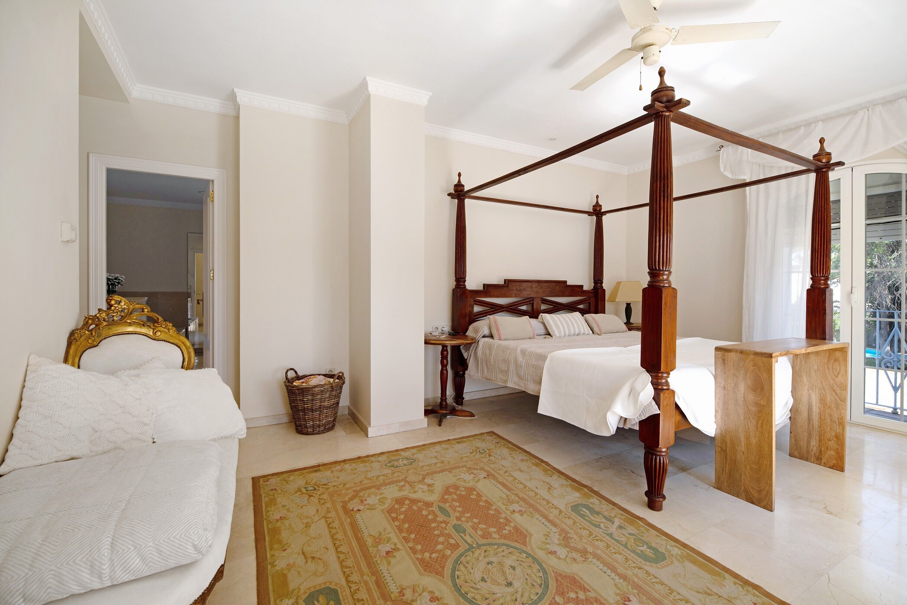 Un dormitorio con cama con dosel, una zona de estar con sofá y un gran ventanal.