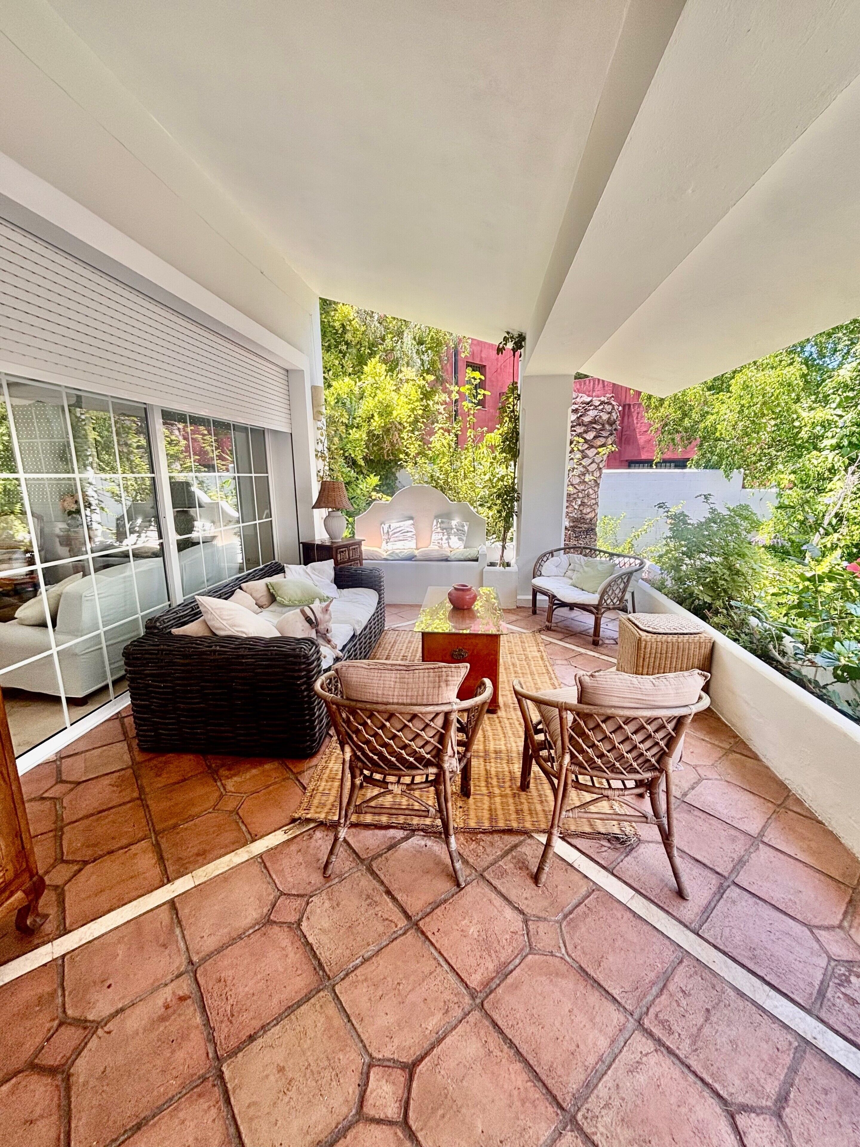 A balcony with wicker furniture, a glass door, and a view of greenery.