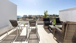 En takterrass med utemöbler, ett glasbord och utsikt över staden och havet.