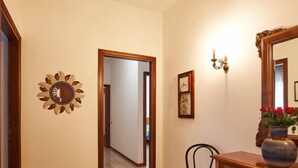 A hallway with a wooden floor, a decorative wall piece, a chair, a wooden dresser, and a mirror. - Massimo by Interhome (Dervio)