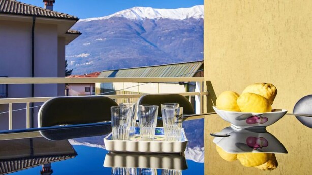A balcony with a table set for two, glasses, and a bowl of lemons. - Massimo by Interhome (Dervio)