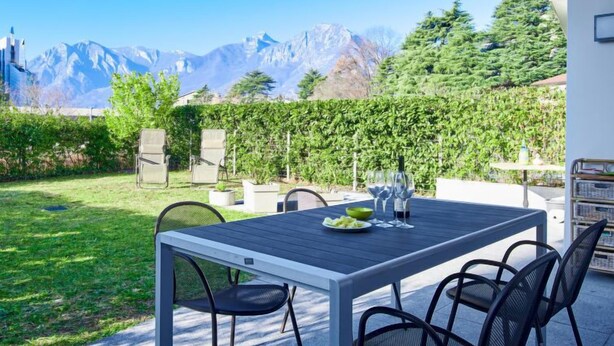 An outdoor patio with a table set for two, surrounded by chairs, and a view of mountains in the background. - Promessi Sposi by Interhome (Lecco)