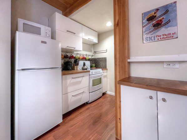 A compact kitchen with white appliances, wooden flooring, and a small countertop.