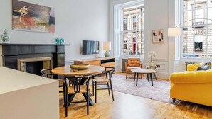 A modern living room with a dining area, a fireplace, and large windows with a city view. - Drake Suite - City Centre 1 Bed Apartment (Edinburgh)