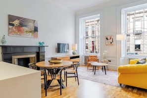 A modern living room with a dining area, a fireplace, and large windows with a city view.