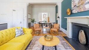 A living room with a yellow sofa, a round coffee table, a fireplace, and a dining area with chairs and a table.