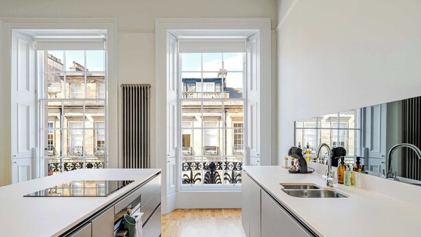 A modern kitchen with white cabinetry, a built-in stove, and a view of a balcony with a wrought iron railing.