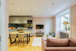 A modern kitchen with a dining area, a TV, and a sofa in a living room.