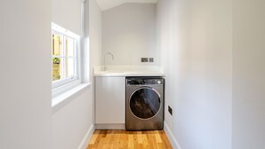 Een kleine wasruimte met een wasmachine, een wasbak en een raam.