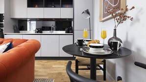 A modern kitchen with white cabinets, a black countertop, and a dining area with a round table set for breakfast. - Wyvern Suite - City Centre 1 Bed Studio Apartment (Edinburgh)