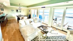 A spacious living room with a large window offering a view of the beach and ocean.