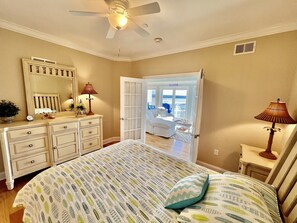 Une chambre à coucher comprenant un lit, une commode, un miroir, un ventilateur de plafond et une porte donnant sur un balcon.