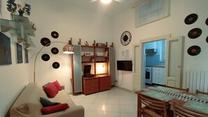 A living room with a sofa, a dining table with chairs, a kitchen area, and a wall decorated with vinyl records. - Comfortable apartment in central area (Bari)