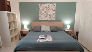 A large bed with a wooden headboard, two bedside tables with lamps, a decorative wall piece, and a built-in shelving unit. - Comfortable apartment in central area (Bari)