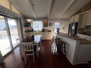 Una cocina con comedor, piso de madera, armarios blancos, un microondas y un ventanal grande.