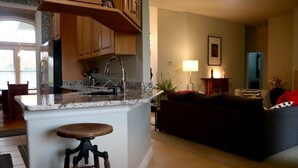 Una cocina con encimera de granito, armarios de madera y refrigerador de acero inoxidable. Hay un taburete frente a la isla de la cocina.